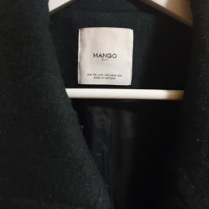 Mörkgrön  kappa från Mango - Elegant mörk grön kappa från Mango med dubbelknäppning och klassisk krage. Perfekt för kyligare dagar med sin stilrena design och långa ärmar.