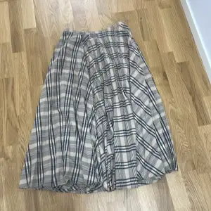 Snygg rutig kjol från H&M i beige och svart. Kjolen har en klassisk design med ett tidlöst rutmönster och är perfekt för både vardag och speciella tillfällen. Den är gjord i ett lätt och bekvämt material som ger en fin passform.