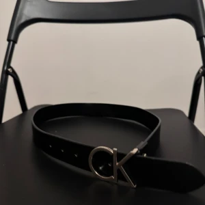 Svart bälte från Calvin Klein - Snyggt svart bälte från Calvin Klein med ett stilrent CK-spänne i silver. Perfekt för att ge en elegant touch till din outfit. Tillverkat i skinn och passar både till jeans och kostymbyxor.