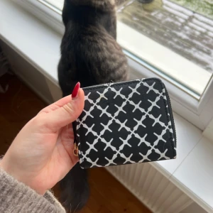 Svart och vit plånbok med mönster - Snygg och kompakt plånbok i svart och vitt med ett stilrent mönster. Plånboken har en praktisk dragkedja i guld som håller dina kort och kontanter säkra. Perfekt för att ha med sig i väskan eller fickan. Aldrig använd 