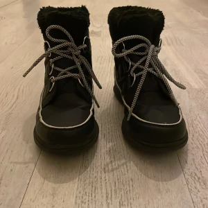Svarta vinterstövlar / kängor från Sorel - Säljer ett par svarta vinterstövlar / kängor från Sorel med snörning och mjukt, varm foder. Perfekta för kalla dagar med sitt robusta material och halkfria sula. Stövlarna har en klassisk design med vit kant och logotyp på sidan.