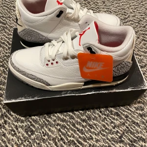 Nike Air Jordan 3 Retro - Säljer ett par Nike Air Jordan 3 Retro i Summit White med detaljer i rött och svart. Skorna har den klassiska elefantmönstrade designen och en synlig Air-enhet i hälen. Perfekta för sneakerentusiaster!
