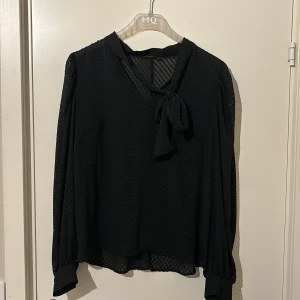 Svart blus i mönster från Stockholm LM - Jätte snygg blus med lite mönster på. En gullig rosett som går att knyta själv vid halsen, knappt använd. Har inga defekter alls