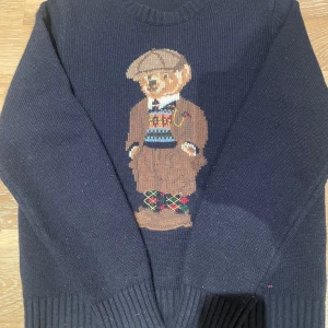 Mörkblå stickad tröja från Polo Ralph Lauren - Säljer en mörkblå stickad tröja med ett charmigt nallemotiv. Perfekt för en mysig och stilren look. Modellen är 171 cm och väger 65 kg. Skriv vid funderingar!