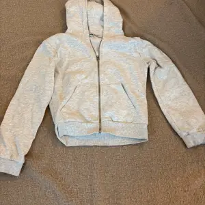 Säljer en bekväm grå hoodie med dragkedja och huva. Perfekt för en avslappnad stil. Den har långa ärmar och en praktisk ficka framtill. Passar bra till vardags.