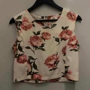 Blommig topp - Ljusrosa blommig topp i fint stumt tyg. Sydd med dragkedja bak hela vägen ner, så den går att öppna helt vilket underlättar på och avklädning. 