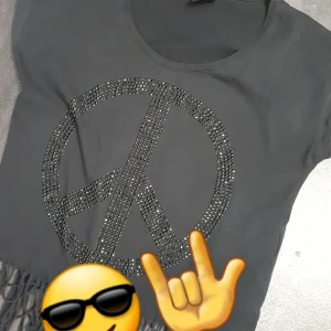 Svart t-shirt med paljetter - Cool svart t-shirt med ett stort paljettmönster i form av ett fredstecken på framsidan. Perfekt för en avslappnad stil med en touch av bling använderintelängre.