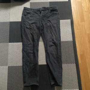 Svarta jeans från Jack & Jones  - Snygga svarta jeans från Rugged med knappgylf och klassisk femficksdesign. Perfekta för en avslappnad stil. Passar bra till både t-shirt och skjorta.