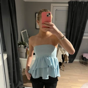 Ljusblå axelbandslös topp från Zara - Säljer en jättefin ljusblå axelbandslös volang topp från zara. 💕säljer den då den aldrig kommit till användning, den finns heller inte längre att köpa 💗