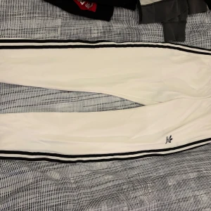 Vita träningsbyxor med svarta ränder - Snygga vita träningsbyxor med svarta ränder längs sidorna. Perfekta för en sportig look. Byxorna har en bekväm passform och är idealiska för träning eller avslappnade dagar.