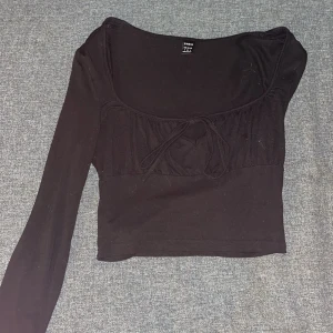 Svart långärmad topp med knyt - Snygg svart långärmad topp med knyt framtill. Toppen har en åtsittande passform och är tillverkad i ett mjukt material.