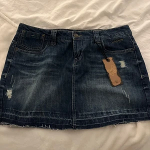 Jeanskjol från Urban Surface - Snygg jeanskjol från Urban Surface i en klassisk blå denim. Kjolen har slitna detaljer och ficksdesign med knapp och dragkedja framtill. Jag är en S beroende på plagg så XL va för stort för mig. Skulle säga att den passar L också 