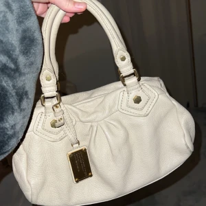 Marc Jacobs väska  - Snygg beige handväska med dragkedja och gulddetaljer. Perfekt för att bära med sig det viktigaste. Stilren och enkel design som passar till många olika outfits. Topp skick med axelremsband som tillkommer❤️från Marc Jacobs. Intressekoll för bästa bud. 