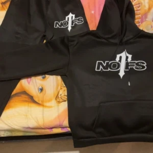 Svart hoodie med tryck - Snygg svart hoodie med ett stort tryck på framsidan. Hoodien har en klassisk design med dragsko i huvan och en stor ficka framtill. Perfekt för en avslappnad stil.