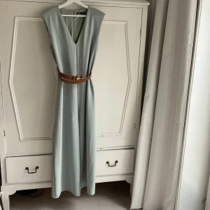 Ljusgrön jumpsuit från Zara - Snygg ljusgrön jumpsuit från Zara med v-ringning och ett brunt bälte i midjan. Böljande och svalt material. Som att bära en skön pyjamas. Tunna axelvaddar ger en snygg siluett. Längd 143 cm. Aldrig använd. 