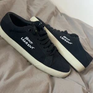 Svarta sneakers från Saint Laurent - Snygga svarta sneakers från Saint Laurent med vit sula och märkets logga i vitt på sidan. Skorna har snörning och en klassisk design som passar perfekt till vardagsstilen. Använd fåtal gånger 