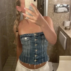 Jeans korsett-topp - Snygg jeans korsett-topp med knappar framtill. Den har en cool design med fickdetaljer och är perfekt för en trendig look. Passar bra till både kjol och byxor. Storlek S. Säljer då den inte kommit till användning och lägger ut annonsen igen💕💕💕
