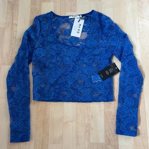 Blå spetströja från NA-KD - Superfin blå spetströja från NA-KD med knappar framtill. Blusen har långa ärmar och ett vackert blommigt mönster!💙 Lite liten i storleken, mer som S/M 