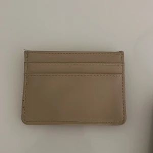 Beige plånbok - Säljer en stilren beige plånbok i skinn med flera kortfack. Perfekt för att hålla ordning på dina kort och kontanter. Enkel och smidig design som passar i alla fickor.