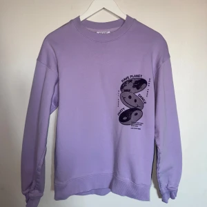 Lila sweatshirt från Vailent - Säljer en cool lila sweatshirt från Vailent med tryck av smileys och texten 'Rave Planet' på både fram- och baksidan. Tröjan har långa ärmar och en avslappnad passform. Perfekt för dig som gillar unika och uttrycksfulla plagg! 