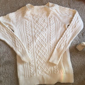 Vit stickad tröja från GAP - Säljer en stilren vit stickad tröja från GAP med ett snyggt flätmönster. Tröjan har långa ärmar och ribbade kanter vid ärmslut och nederkant. Perfekt för kyliga dagar!