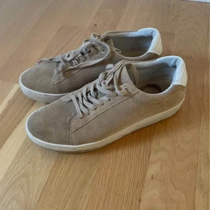 Beige mockasneakers från Vagabond - Snygga beige sneakers i mocka från Vagabond med vit sula och snörning. Perfekta för en stilren look. De har en diskret design med en vit detalj vid hälen.