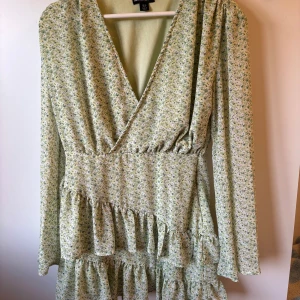 Blommig volangklänning grön S - Söt klänning i ljusgrön färg. Klänningen har en omlott-design med volanger och långa ärmar. Perfekt för vår och sommar! 🌸🪷 Fint skick!