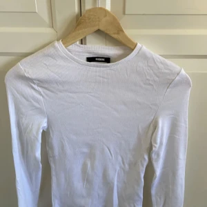 Vit ribbad långärmad topp från Bik Bok - Säljer en stilren vit ribbad topp från Bik Bok. Den har långa ärmar och en rund halsringning, perfekt för lager-på-lager eller som den är. Passar till många olika outfits!