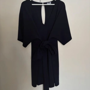 Marinblå klänning från Make Way - Elegant mörk blå klänning från Make Way med v-ringning och knytband i midjan. Tillverkad i polyester och elastan för en bekväm passform. Perfekt för en stilren look.