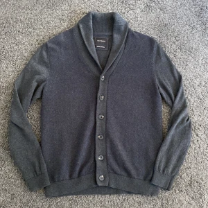 Stickad cardigan med Kashmir - Säljer en stilren grå kofta från Westbury i bomull och kashmir. Koftan har en klassisk design med knappar framtill och ribbade muddar. Perfekt för en avslappnad men ändå elegant look. Helt ny skick 9,9/10 använd en gång. Modellen är 186 och den sitter perfekt. Priset är ej hugget i sten så kom med prisförslag. Skriv för fler frågor eller bilder👍