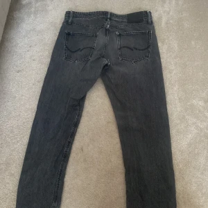 Svarta jeans från Jack & Jones - Säljer ett par svarta jeans från Jack & Jones i loose fit. De har en klassisk femficksdesign och knappar i gylfen. Perfekta för en avslappnad stil.