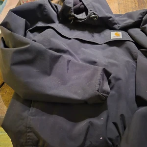 Svart jacka från Carhartt - Säljer en svart jacka från Carhartt med huva och dragkedja. Perfekt för kyligare dagar. Jackan har en enkel och stilren design med långa ärmar.lite färg dock på små ställen.Men helt cool annars.