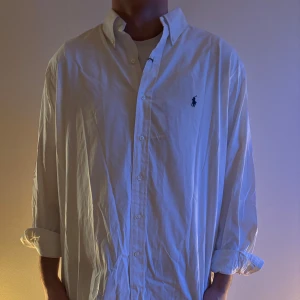Vit skjorta från Ralph Lauren - Klassisk vit skjorta från Ralph Lauren med lång ärm och knappstängning. Den har en broderad logotyp på bröstet och är tillverkad i bomull. Perfekt för en stilren look.