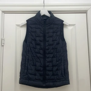 Svart quiltad dunväst - Snygg svart quiltad dunväst från Everest . Perfekt för lager-på-lager under kyliga dagar. Västen har en dragkedja framtill och en stilren design.