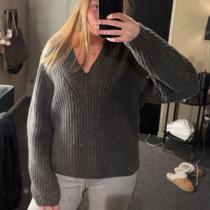Grå stickad tröja - Mysig grå stickad tröja med v-ringning. Perfekt för kyliga dagar och ger en avslappnad look. Tröjan har långa ärmar och en bekväm passform.