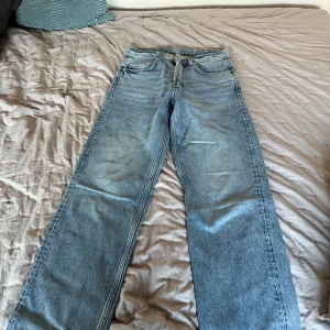 Blå jeansbyxor - Säljer ett par klassiska blå jeansbyxor med en straight passform. Byxorna har en midwaist design och är utrustade med  knappar. Perfekta för en avslappnad stil.