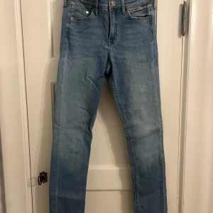 Blå jeans  - Snygga blå jeans med klassisk femficksdesign och knappgylf. De har en normal passform och är perfekta för en avslappnad stil. Jeansen har en lätt tvättad look som ger dem en trendig touch. Strl 26/30