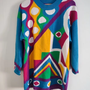 Färgglad stickad tröja  - Säljer en unik och färgglad stickad tröja med ett geometriskt mönster i blått, gult, grönt, rosa och vitt. Tröjan har långa ärmar och en rund halsringning. Är ganska lång så kan användas som klänning också.