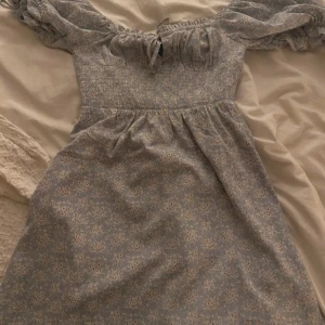 Blommig klänning från NA-KD - Söt blommig klänning från NA-KD i ljusblått med små blommor. Klänningen har korta ärmar med volangdetaljer och en smockad överdel som ger en fin passform. Perfekt för en somrig look!