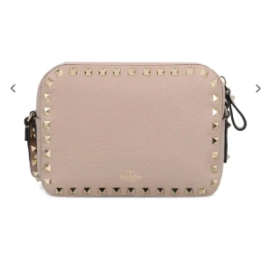 Beige axelväska från Valentino - Tänkte kolla intresset på min snygga beiga axelväska från Valentino med guldfärgade nitar runt kanterna. Väskan har en justerbar axelrem och är perfekt för att ge din outfit en edgy touch. Tillverkad i skinn för en lyxig känsla. Den är i nyskick.