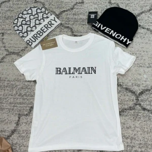 Vit t-shirt från Balmain - Säljer en stilren vit t-shirt från Balmain med svart texttryck på bröstet. T-shirten har en klassisk rund hals och korta ärmar. Perfekt för en trendig och avslappnad look.