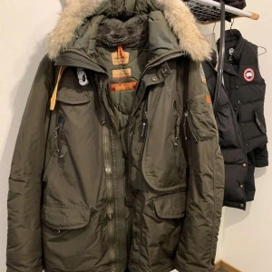  Parajumpers Right Hand XL - Säljer en grön parkajacka från Parajumpers med pälsfodrad huva och flera praktiska fickor. Jackan har en quiltad insida och dragkedja framtill. Perfekt för kalla dagar.