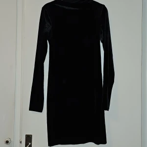 Svart sammet klänning - Elegant svart klänning i mjukt sammetstyg. Den har en klassisk design med långa ärmar och en figurnära passform. Perfekt för en stilren look.