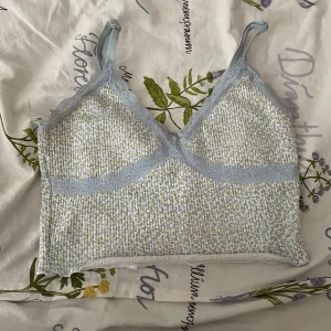 Blommig linnetopp med spetsdetaljer - Söt linnetopp med blommigt mönster i ljusblått och grönt. 🩷