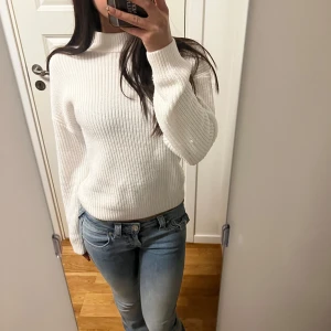 Vit stickad tröja - Säljer en stilren vit stickad tröja med ribbad struktur. Tröjan har långa ärmar och en klassisk passform som passar perfekt för kyligare dagar. Perfekt att matcha med jeans för en avslappnad look.