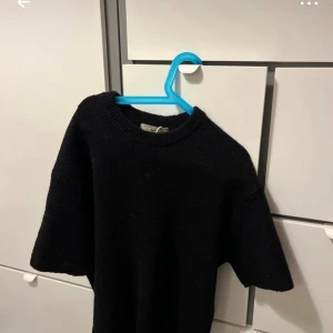 Svart stickad tröja - Säljer en stilren svart stickad tröja med korta ärmar. Perfekt för en avslappnad look. Tröjan har en rund halsringning och är gjord i ett mjukt material.