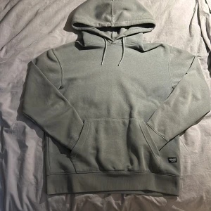 Olivgrön hoodie från Jack & Jones - Säljer en stilren olivgrön hoodie från Jack & Jones. Den har en klassisk design med en stor ficka framtill och justerbar huva. Perfekt för en avslappnad look.