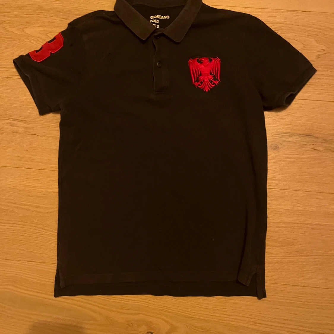 Svart pikétröja med röd broderad detalj