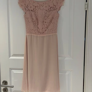 Puderrosa spetsklänning från Zetterberg - Elegant rosa klänning från Zetterberg couture med vacker spetsdetaljering och korta ärmar. Klänningen har en öppen rygg och en mjuk, flödande kjol, som går till knäna. Perfekt för speciella tillfällen, som t ex vårbal. Nypris 3590kr. Aldrig använd. 