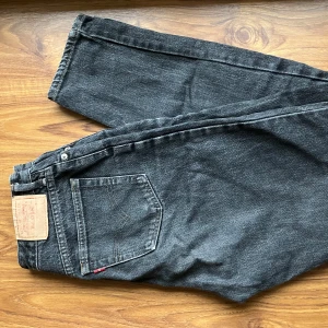 Svarta jeans från Levi's - Snygga svarta jeans från Levi's med klassisk femficksdesign och dragkedja. Perfekta för en avslappnad stil. Märkeslappen syns tydligt på baksidan. Tror jeansmåtten är ungefär W26-27 och L29